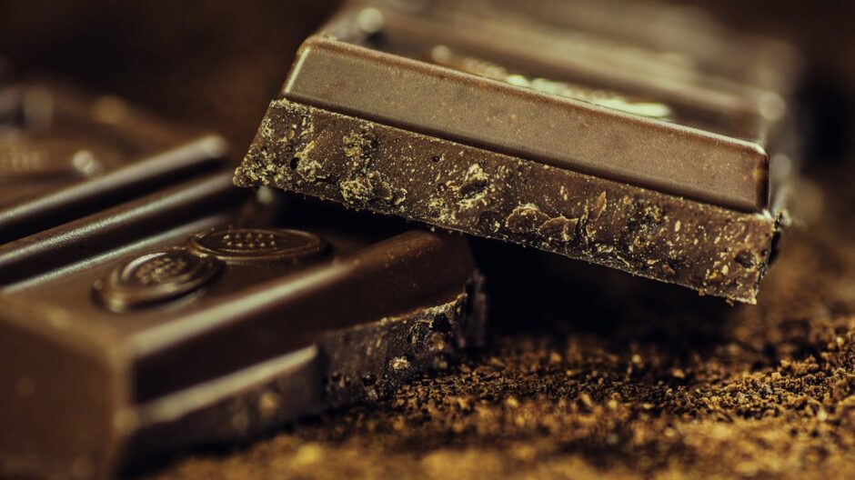 Dark chocolate bars broken into pieces stacked on cocoa powder, close-up macro shot